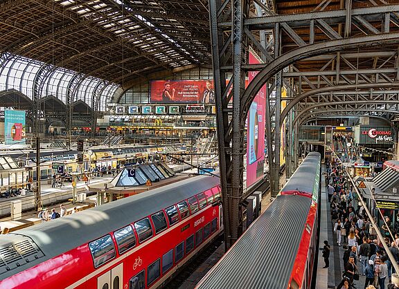 Der Hamburger Hauptbahnhof. Von oben sieht man das Treiben in der Bahnhofshalle mit roten Zügen und überfüllten Bahnsteigen.