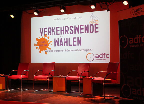 Ein leeres Podium in warmem Licht mit Willkommensbild aus der Leinwand dahiner.