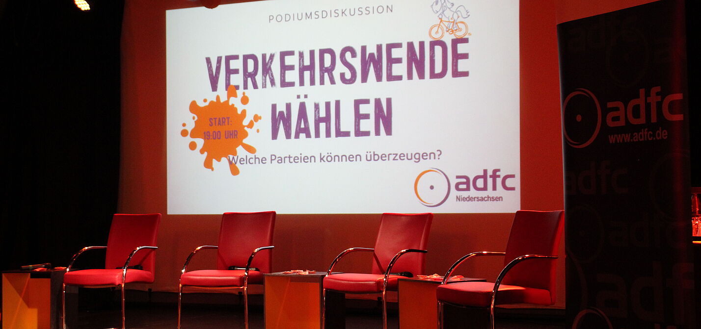 Ein leeres Podium in warmem Licht mit Willkommensbild aus der Leinwand dahiner.