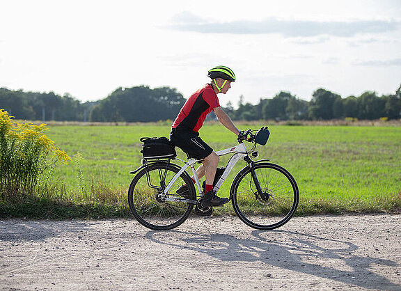 Radfahrer fährt auf einem sportlichen Rad auf einem Radweg vor einer Wieser