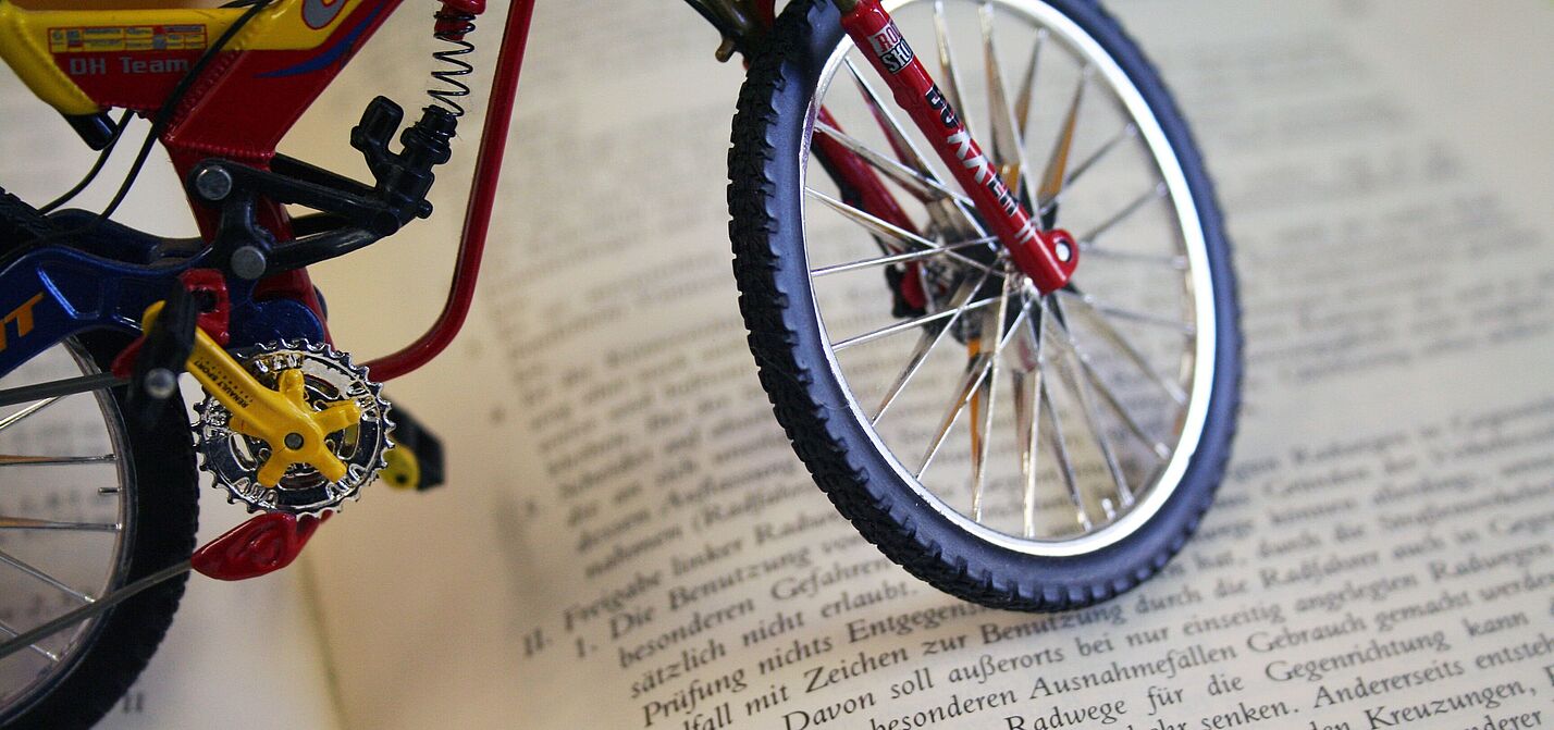 Miniatur-Fahrrad steht auf einem aufgeschlagenen Buch mit deutschem Gesetzestext.